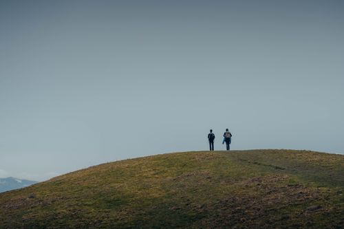 Free Two people hiking on a grassy hill under a clear sky, capturing a sense of adventure. Stock Photo
