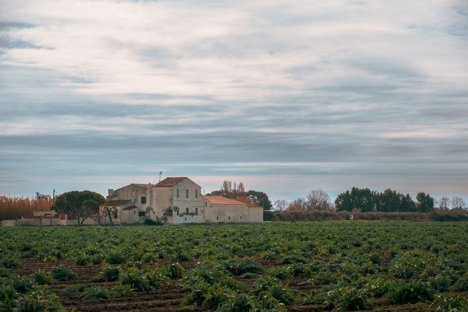 Escena rural con casa de campo y campo en El Prat de Llobregat, España, bajo un cielo nublado.