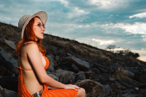 Free Young woman wearing an orange swimsuit and hat, enjoying a day outdoors with a scenic backdrop. Stock Photo
