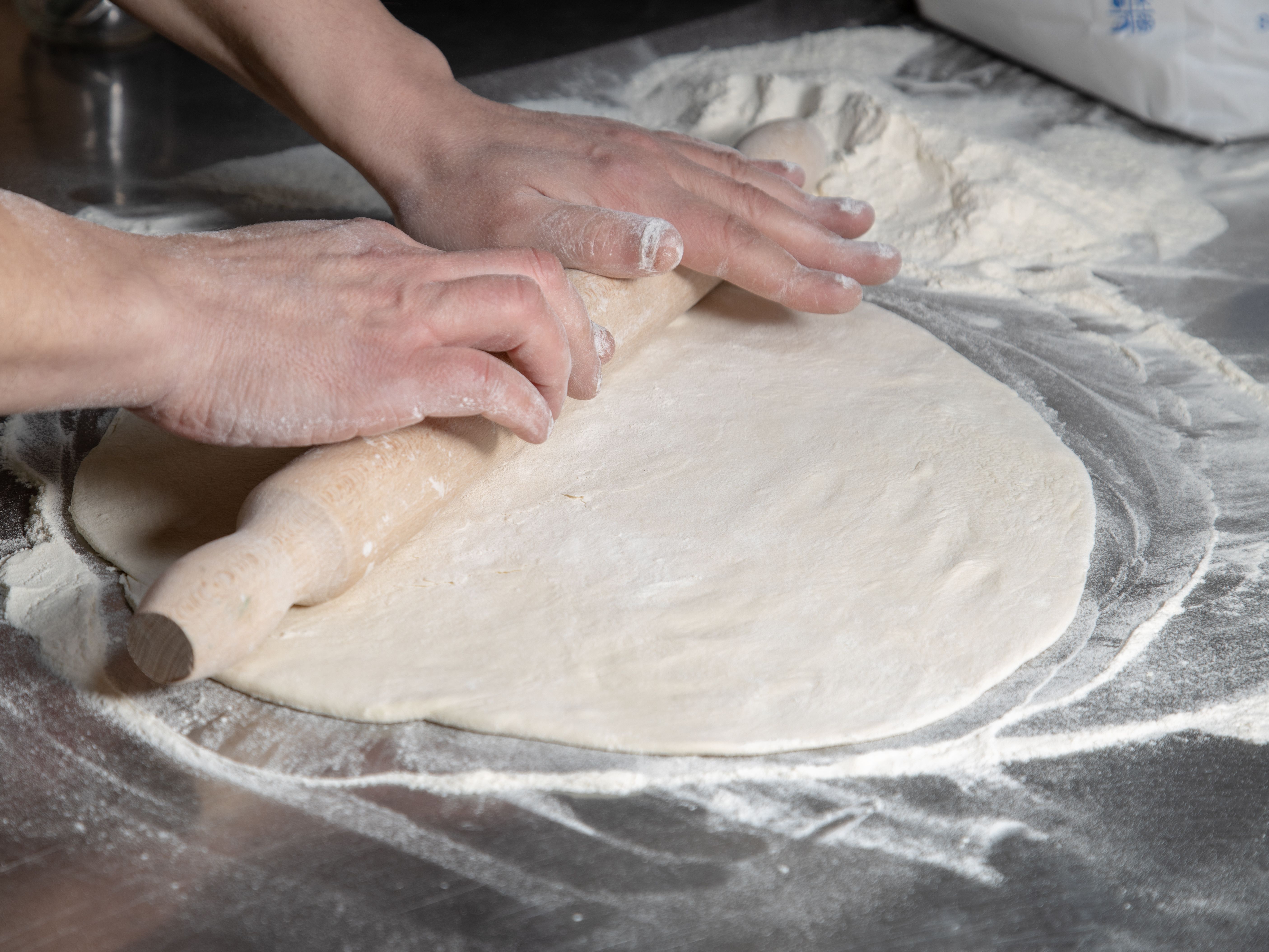 Dough being rolled out on a floured surface with a wooden rolling pin - receita torta de gorgonzola
