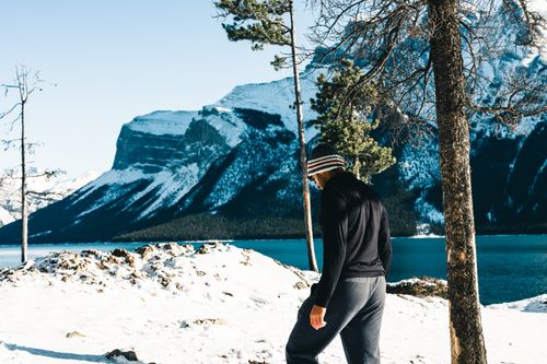 Free A man stands by a snowy lake with mountains in Banff, Canada, during winter. Stock Photo