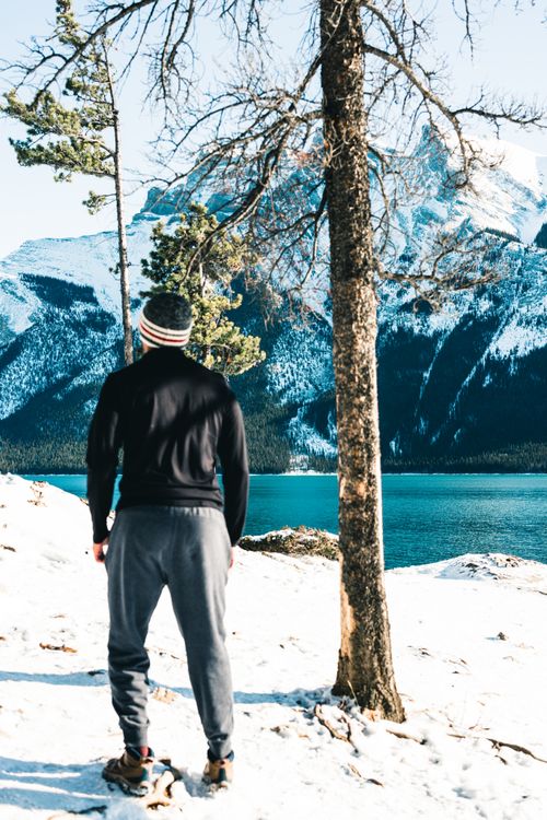 Free A man stands in winter attire, gazing at snowy mountains and a lake in Banff, Canada. Stock Photo