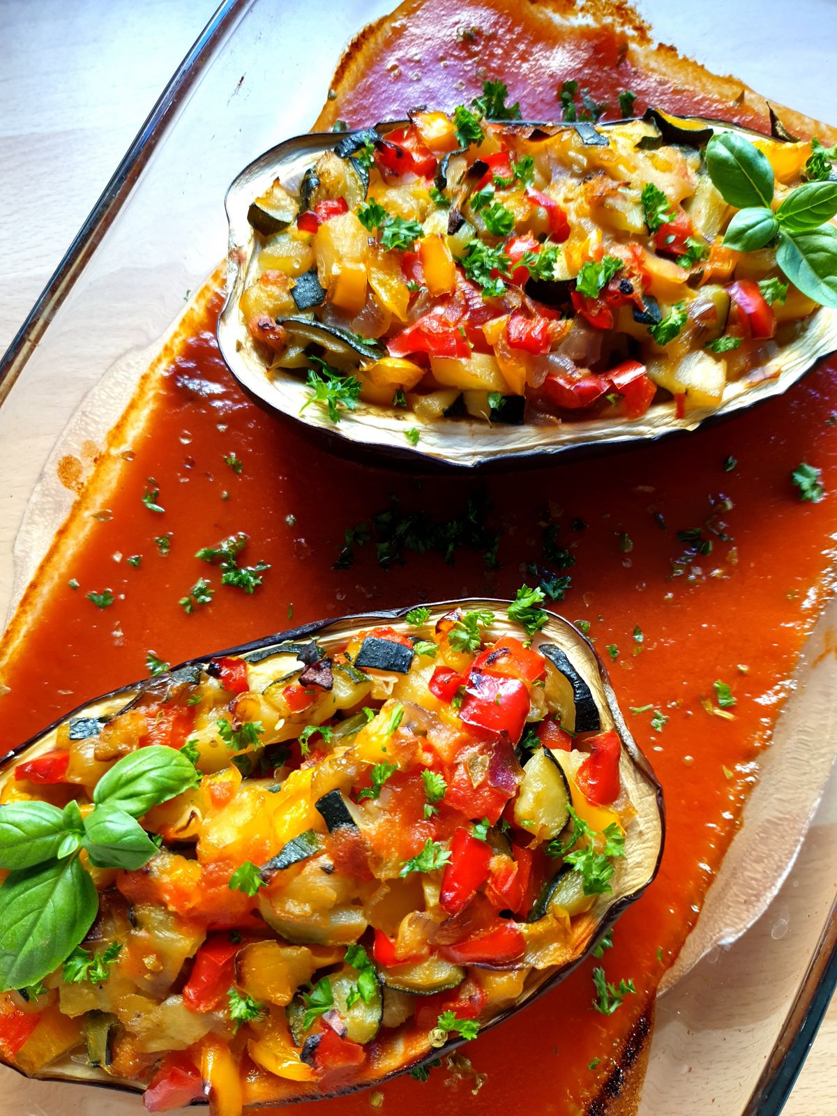 Two eggplant halves filled with diced peppers, zucchini and herbs over tomato sauce