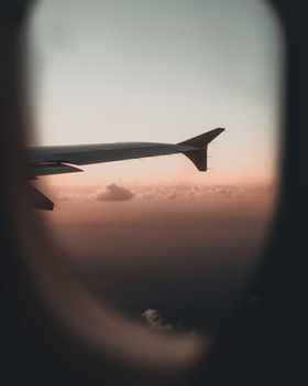 A tranquil view of an airplane wing against a sunset sky through the plane window.