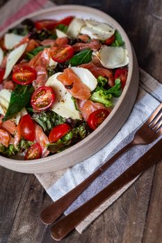 A colorful salmon and goat cheese salad with cherry tomatoes served in a round wooden bowl.