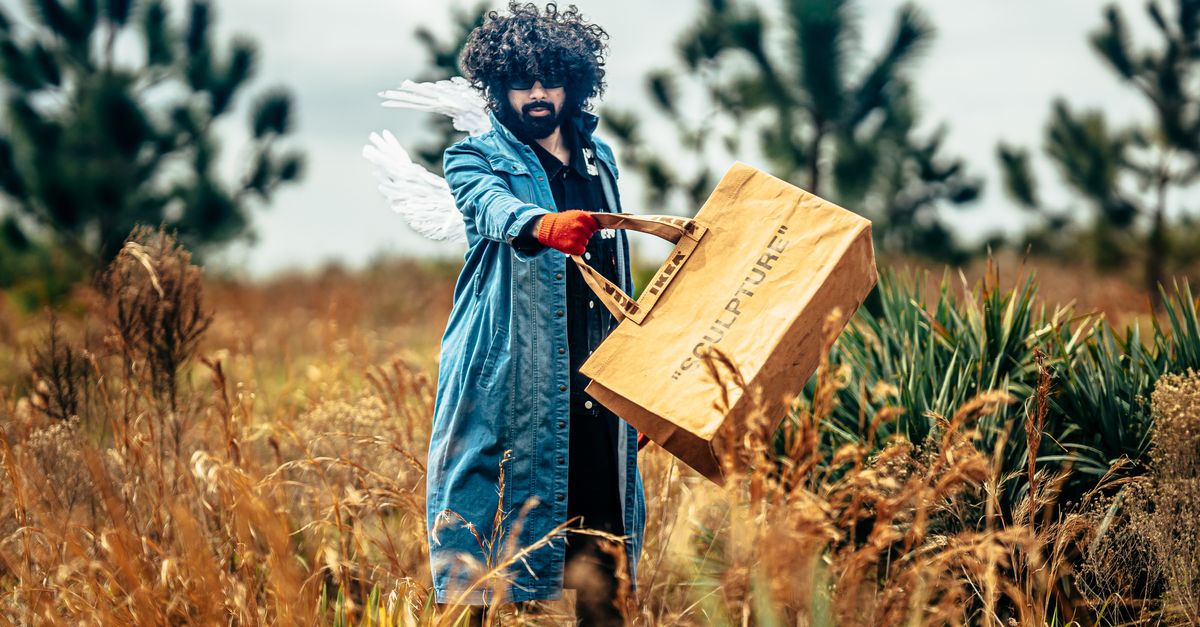 Photo by Jvxhn Visuals Man in denim coat with wings holding wooden box amidst rural field.