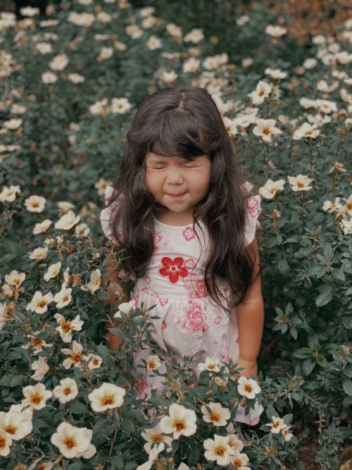 Free A child in a flower-filled meadow with eyes closed, embracing nature. Stock Photo