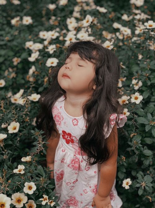 Free Young girl stands with eyes closed among blooming flowers in a meadow. Stock Photo