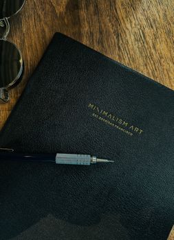 A minimalist black folder with text, a pen, and sunglasses on a wooden surface, highlighting simplicity.
