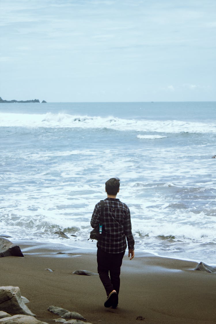 Man With A Camera Walking On An Empty Beach In Windy Weather 