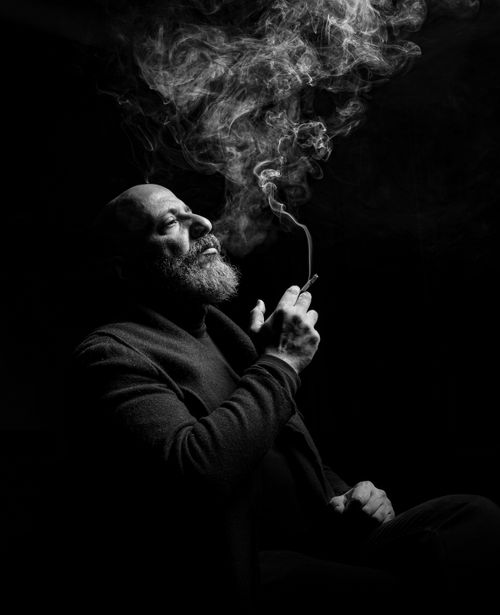 Free Elegant black and white portrait of a thoughtful man smoking in a studio setting. Stock Photo