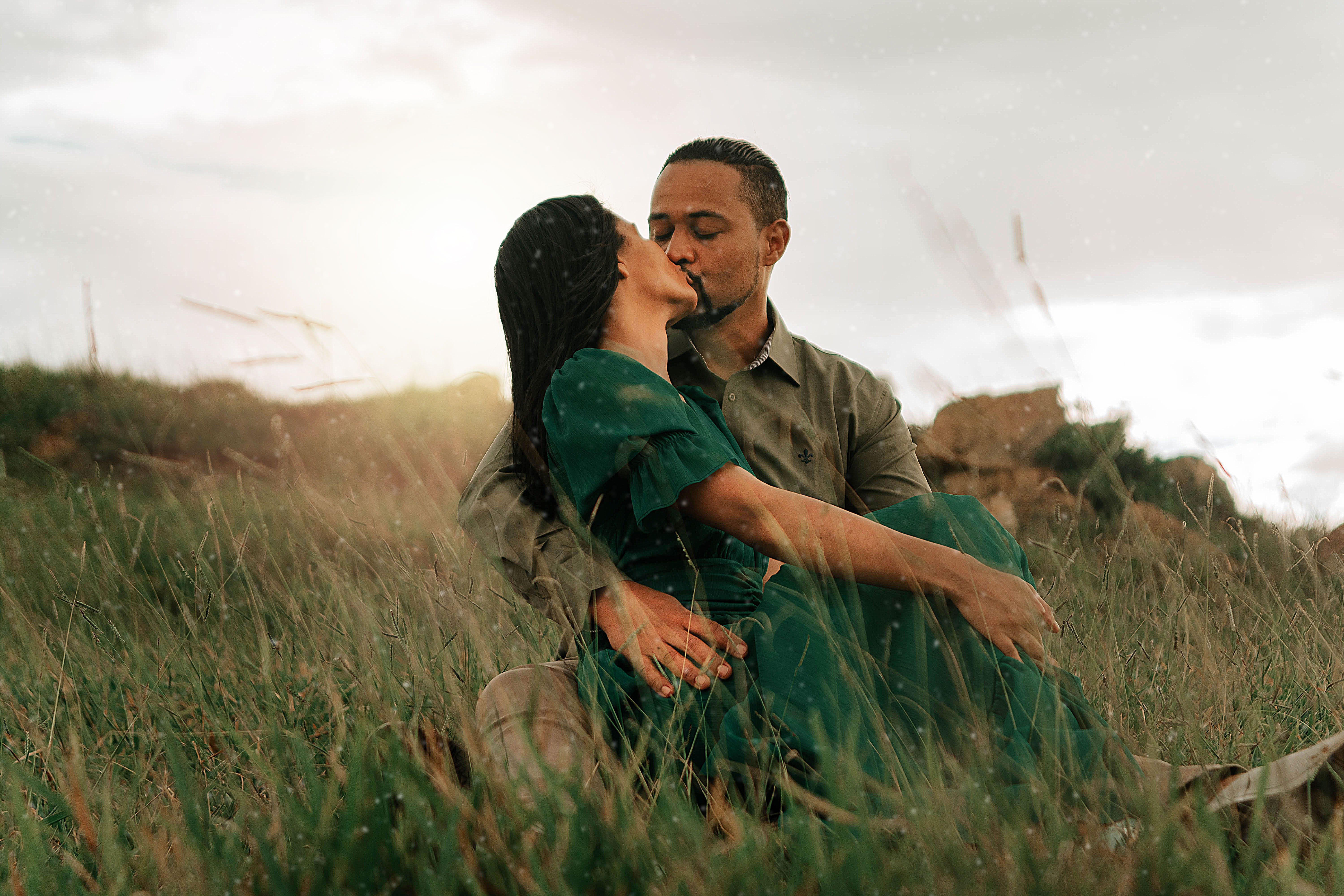 A couple sharing a romantic kiss outdoors in a lush green field during summer.