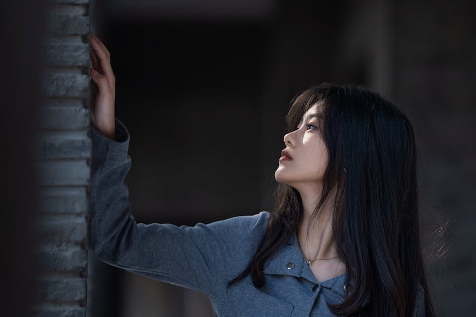 Side profile of a woman touching a wall, deep in thought, indoors.