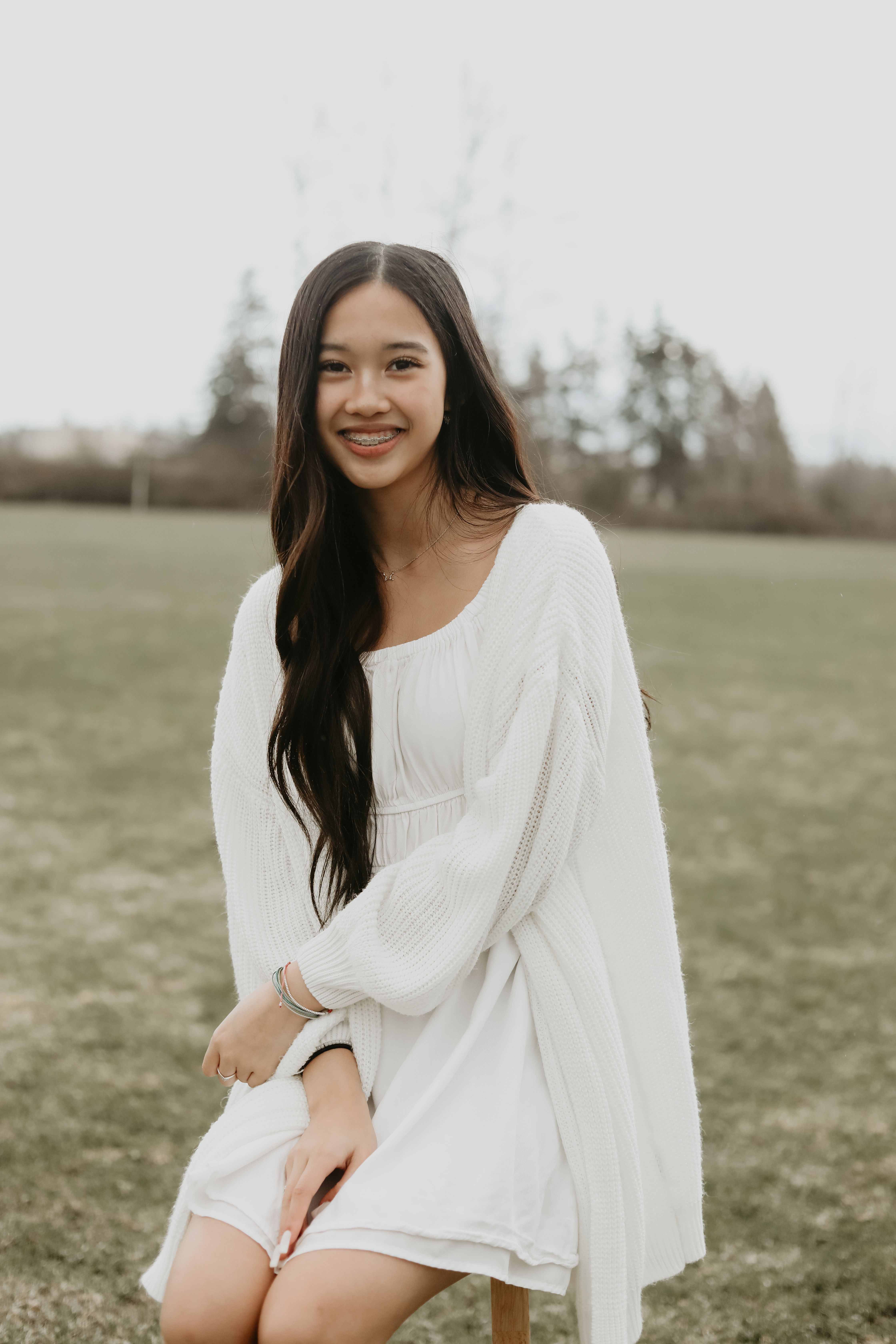 Asian woman sitting outdoors in a white dress, smiling warmly