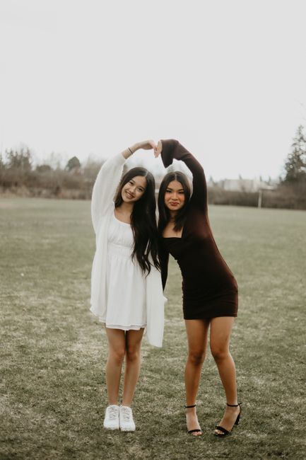 Two young women in stylish dresses posing playfully on a grassy field outdoors.
