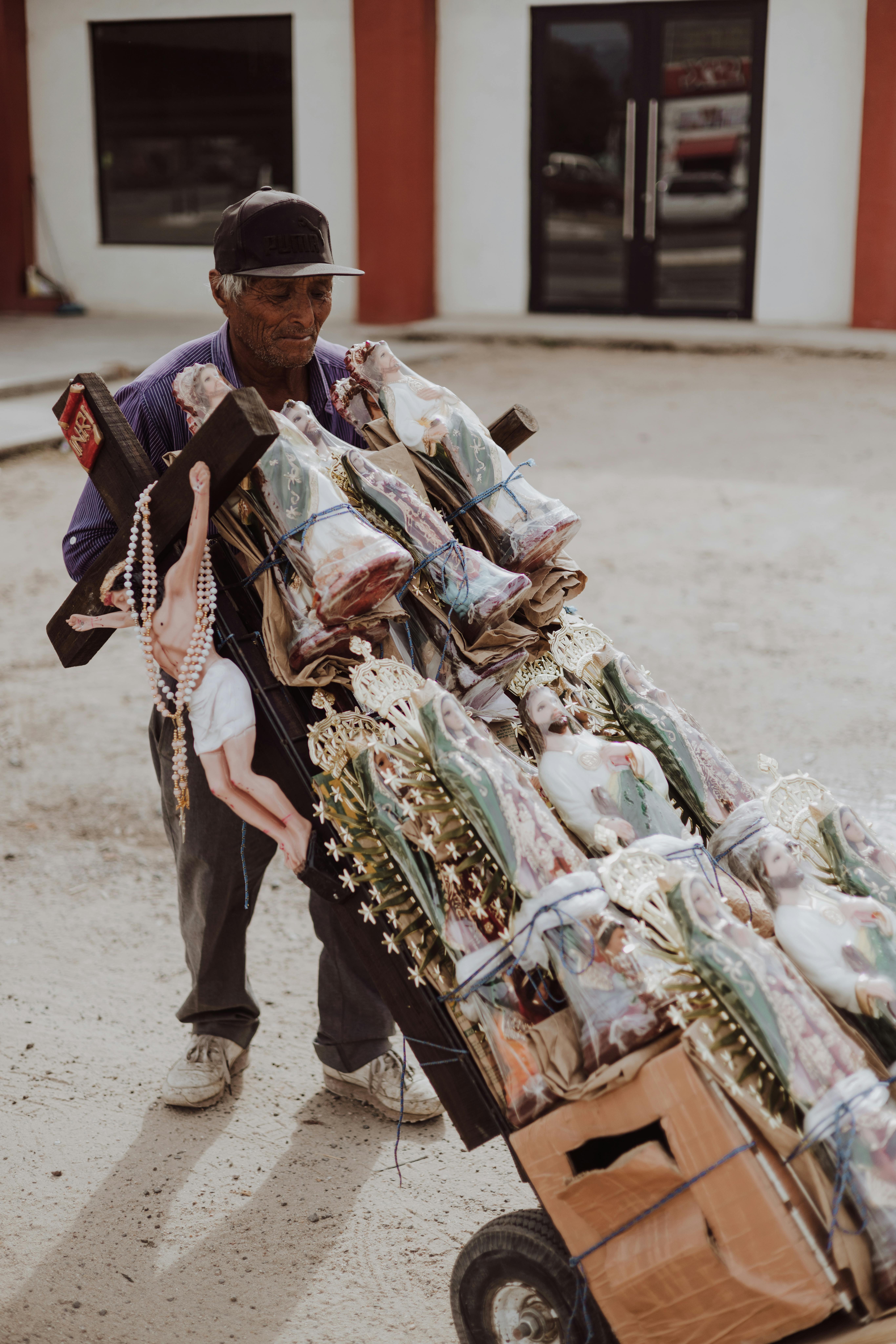 An elderly man pushes a cart full of religious statues outdoors, showcasing cultural traditions.