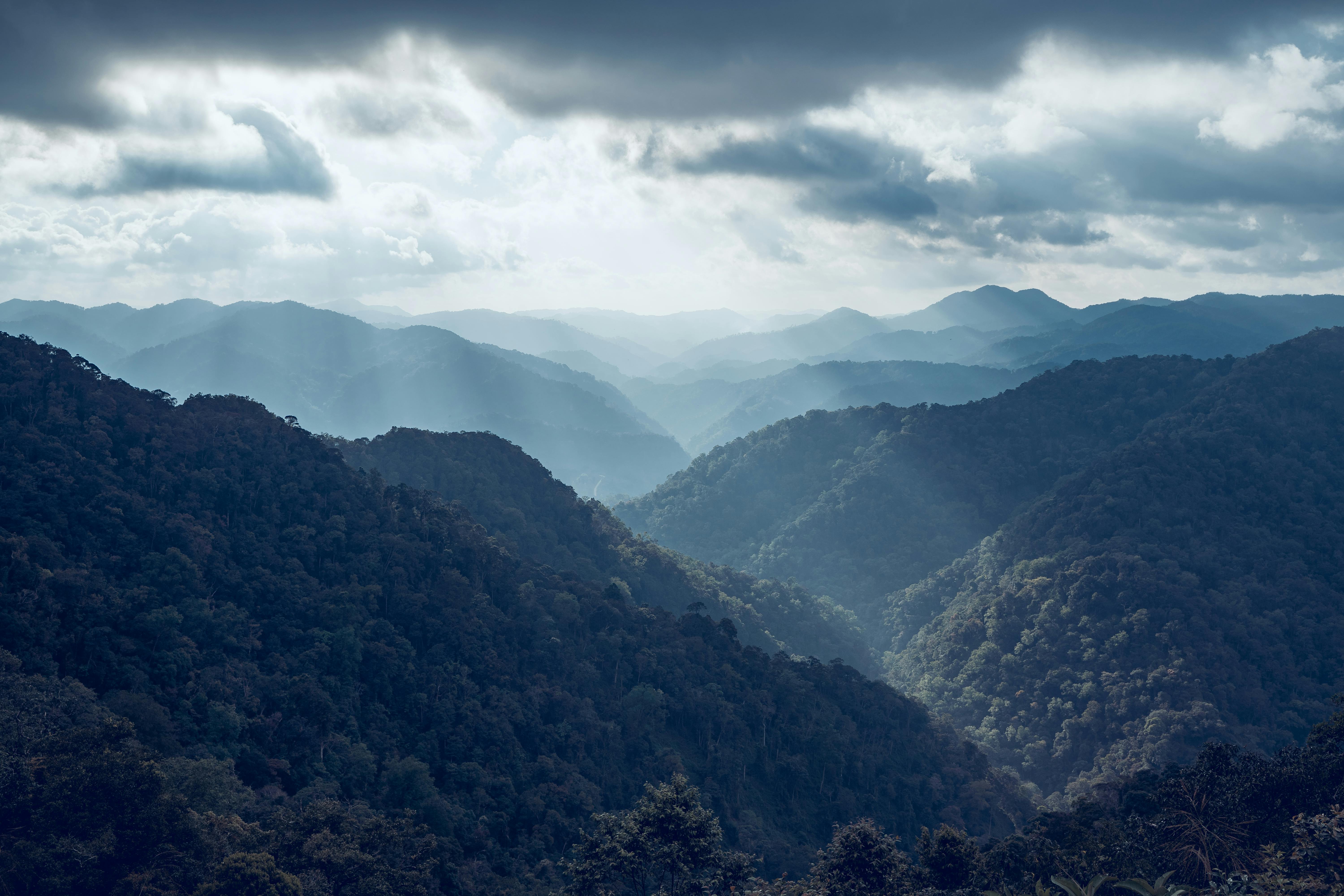 Free Stunning aerial view of mountains with sun rays streaming through clouds, creating a dramatic scene. Stock Photo