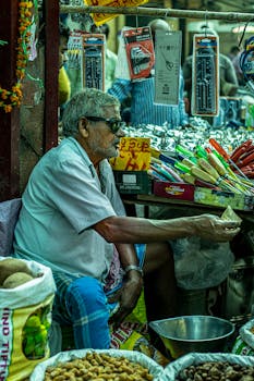 An elderly man sells vegetables and fruits at a vibrant market stall in Delhi, India.