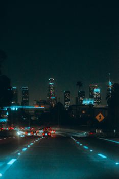 A city skyline at night with illuminated skyscrapers and a busy highway leading into the urban core.