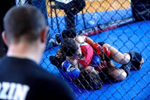 Free Two women competing in a mixed martial arts training session inside a gym cage with a coach observing. Stock Photo