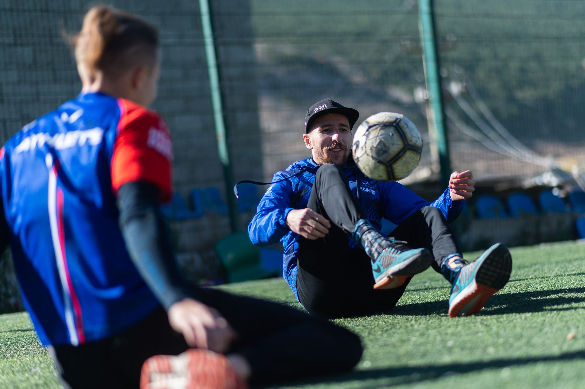 Two soccer players in sportswear practicing ball control outdoors on a sunny day.
