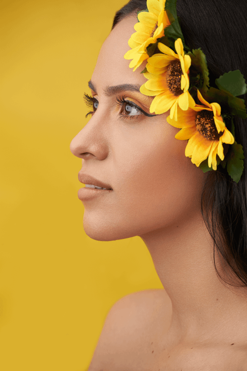 Free A woman adorned with a sunflower garland smiles against a vibrant yellow background. Stock Photo