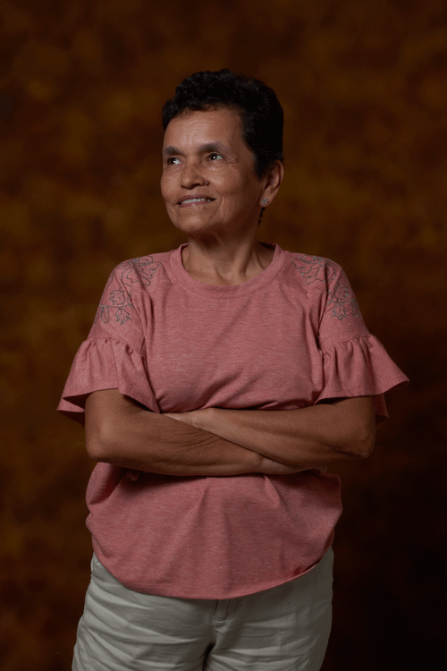 Free Smiling Hispanic woman with short hair, wearing casual pink shirt, posing against a dark background. Stock Photo
