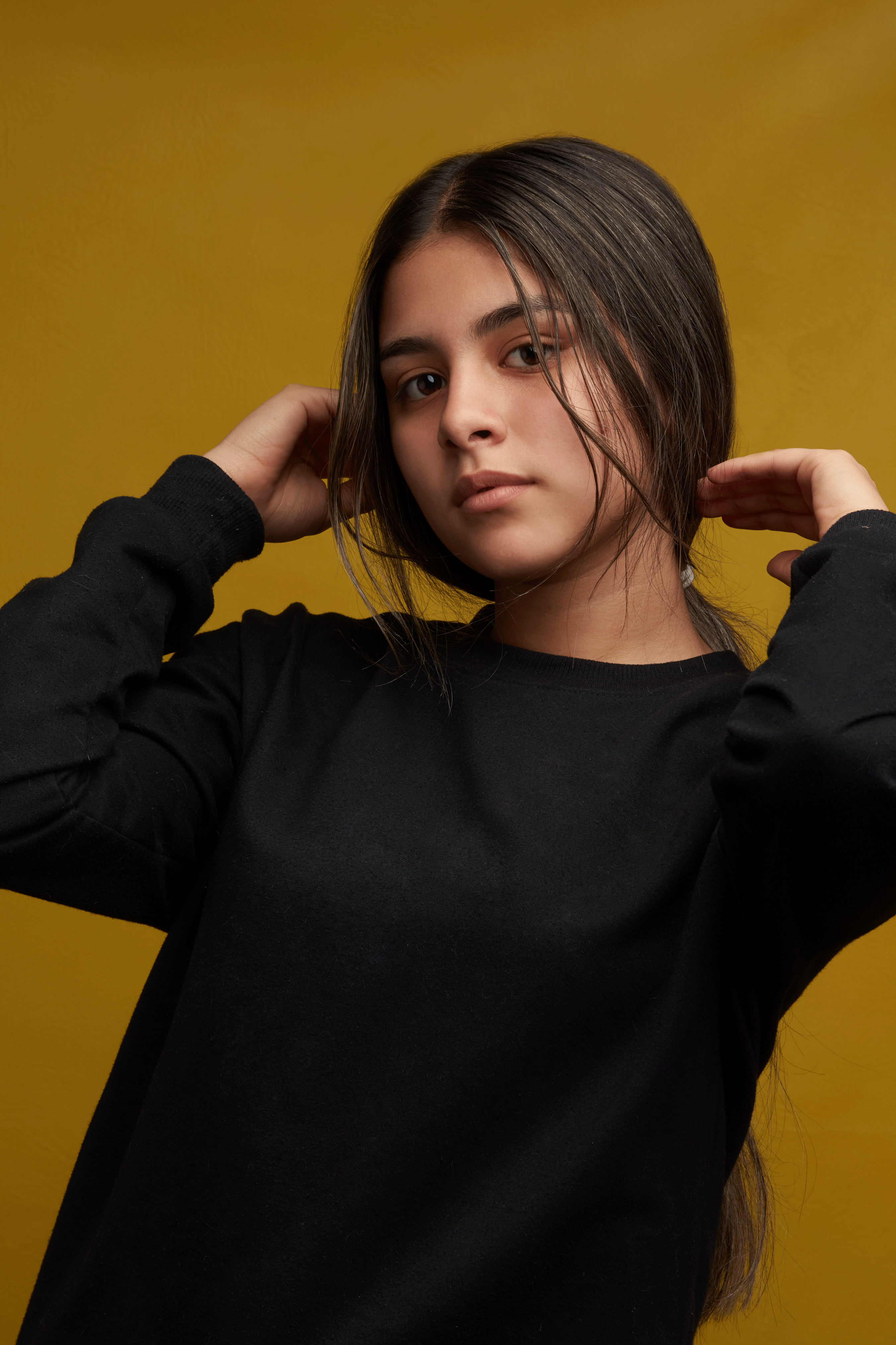 Studio portrait of a young woman posing in casual clothing with a yellow backdrop.