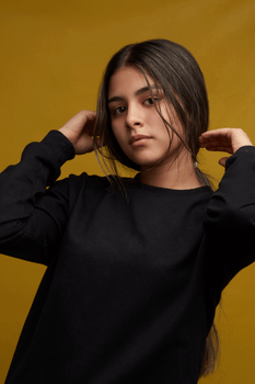 Studio portrait of a young woman posing in casual clothing with a yellow backdrop.