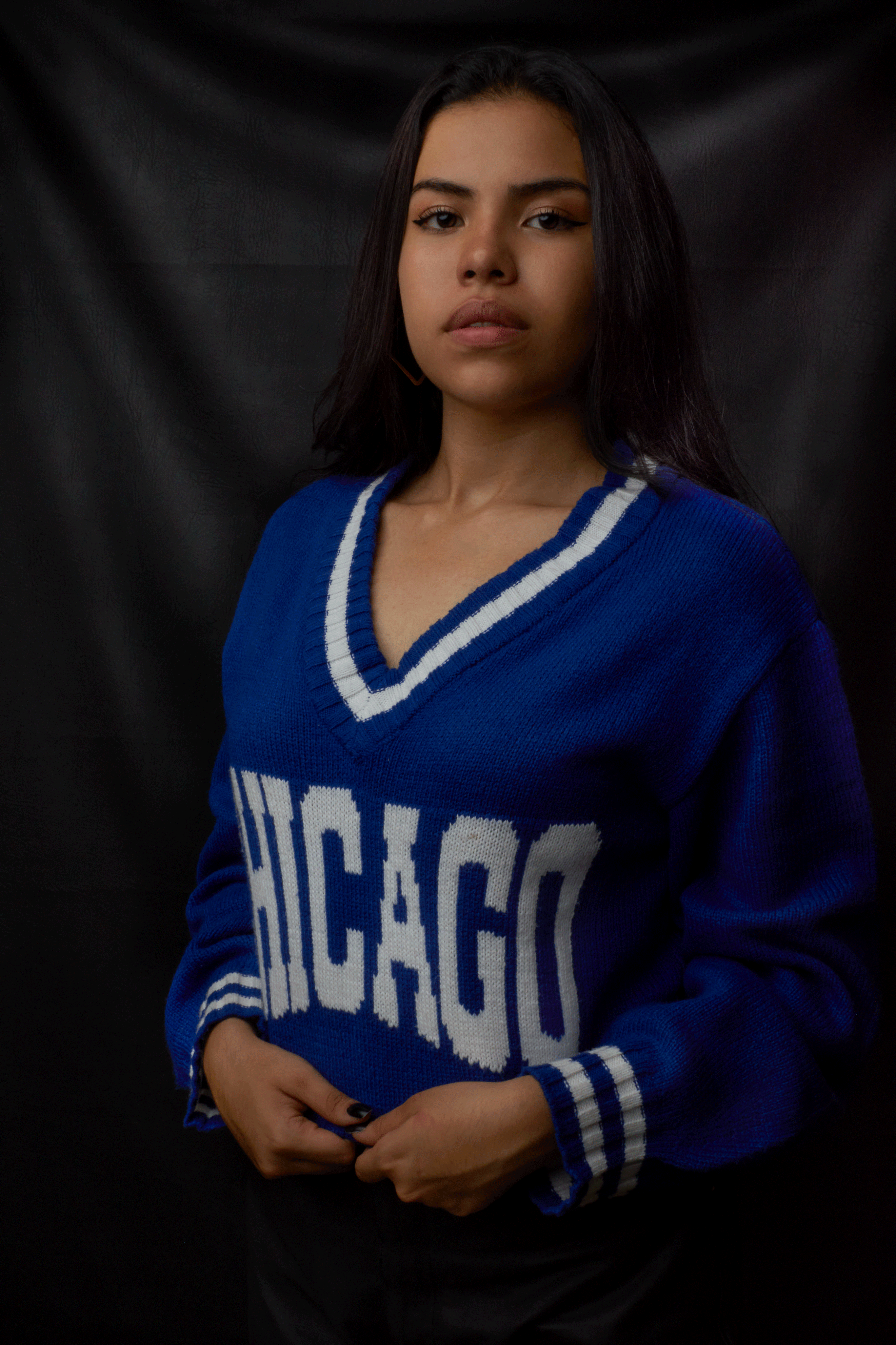 Woman standing in studio wearing a blue Chicago sweater with a black background.