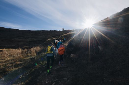 A group of hikers with backpacks moving up a mountain trail under bright sunlight.