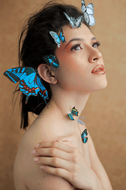 Free Artistic portrait of a woman with vibrant blue butterflies on a brown background. Stock Photo