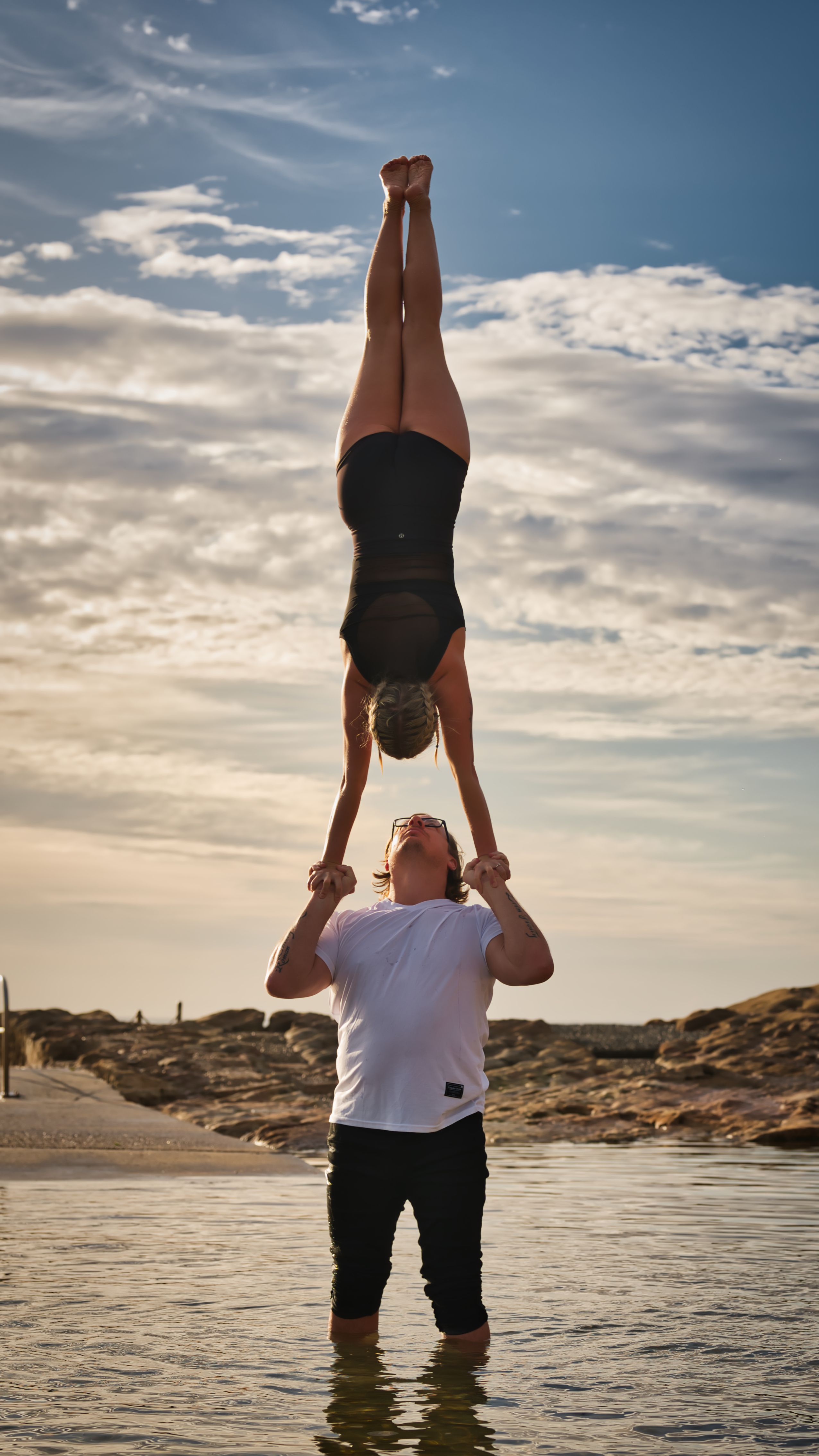 A couple performing an impressive acrobatic stunt, showcasing strength and balance, against a scenic lake backdrop.
