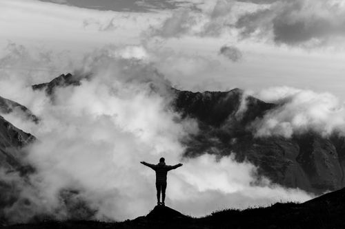 Free A lone hiker silhouetted against majestic mountains and swirling clouds, embracing nature's grandeur. Stock Photo