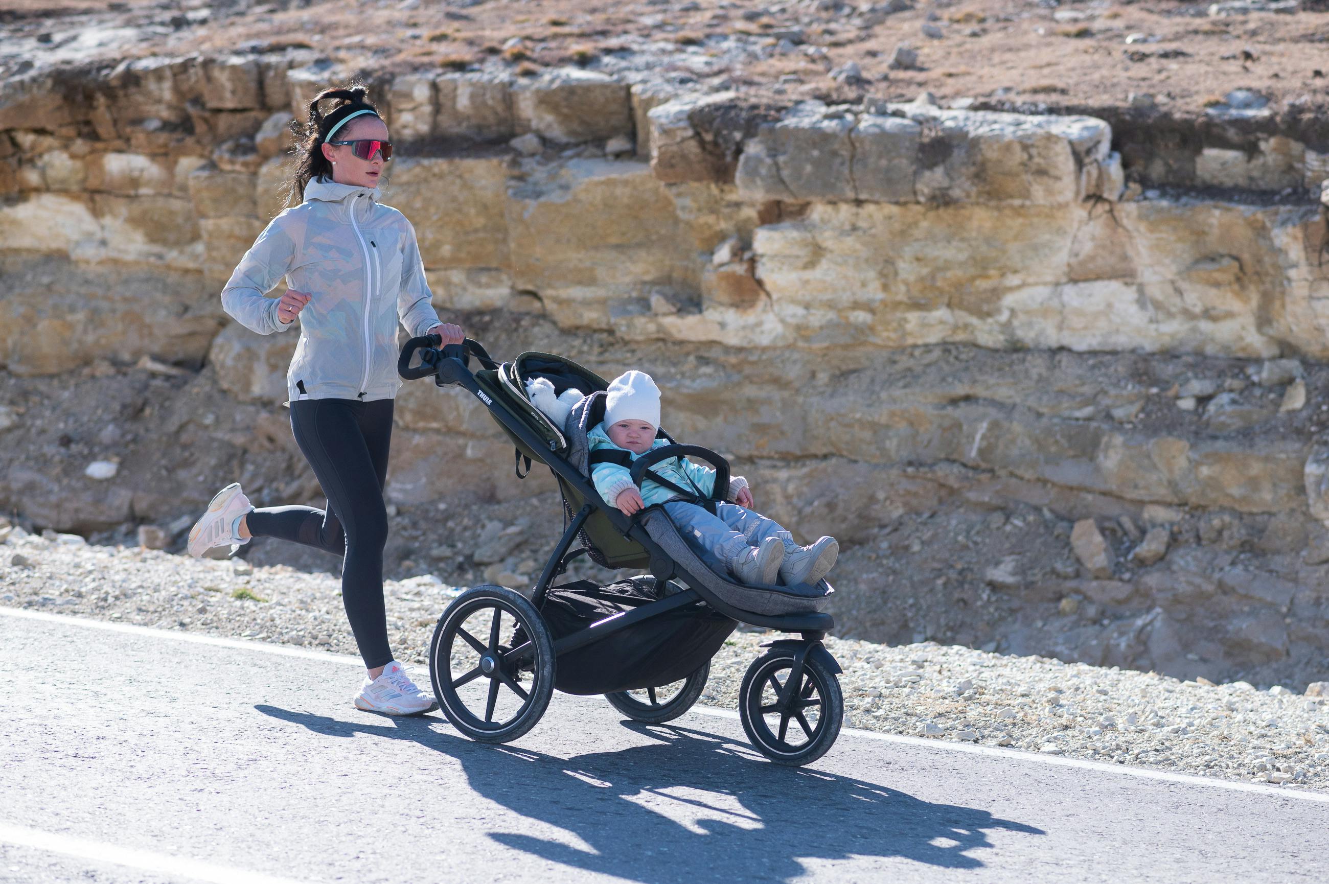 woman in sportswear running with stroller with child