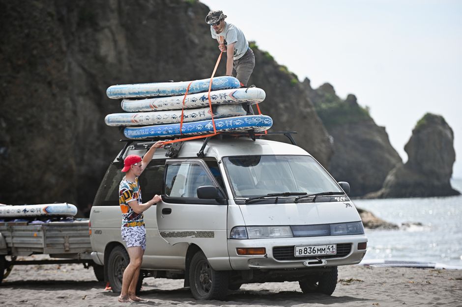 Two men loading surfboards onto a van by a rocky beach, preparing for a summer adventure.