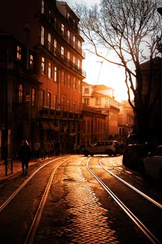 Golden sunset casts warm hues over a cobblestone street in Lisbon, Portugal.