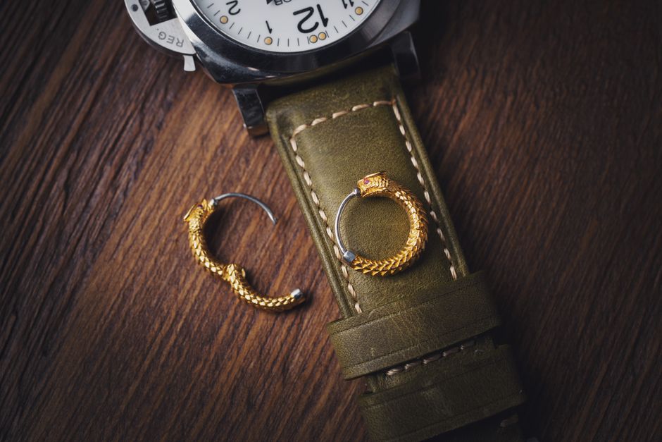 Elegant wristwatch with gold snake earrings on a leather strap, showcasing luxury details.