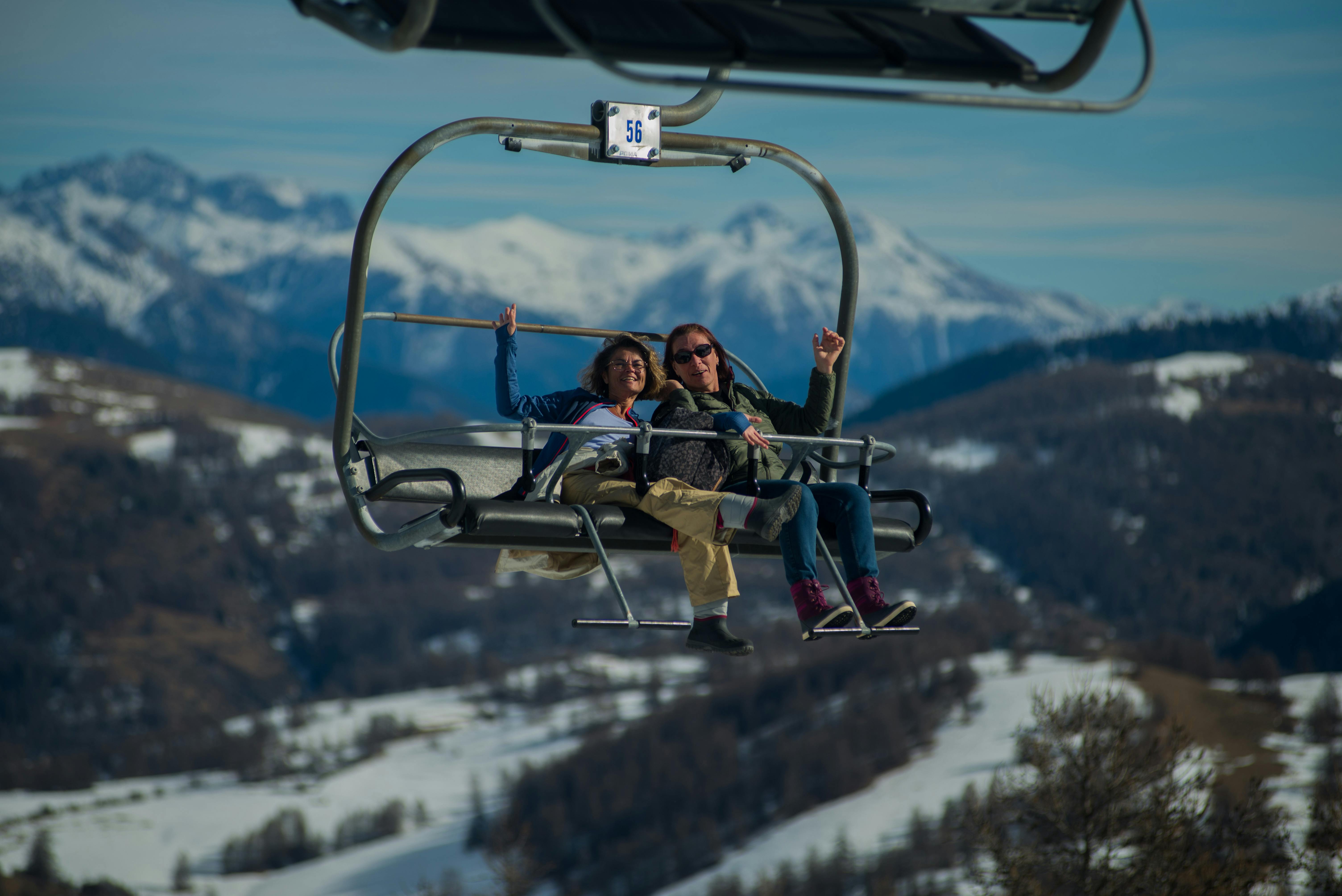 Happy couple on a ski lift surrounded by snowy mountains, capturing a joyful winter adventure.