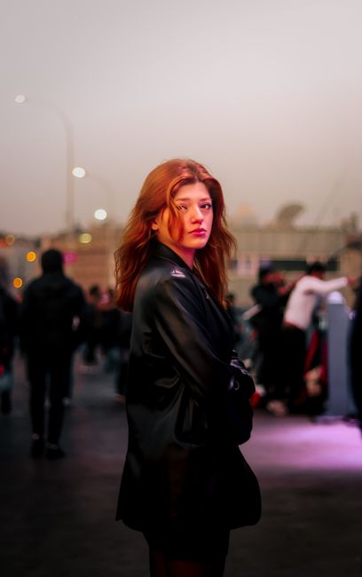 Portrait of a woman in a leather jacket standing in a bustling night street.