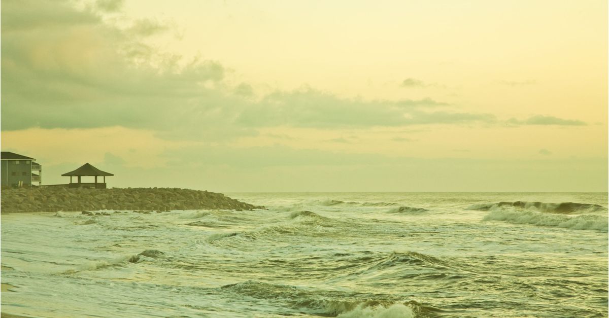 A serene beach view at sunset with gentle waves and a cloudy sky.