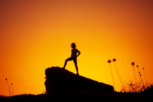 Free A striking silhouette of a girl standing on a rock against a vibrant sunset sky. Stock Photo