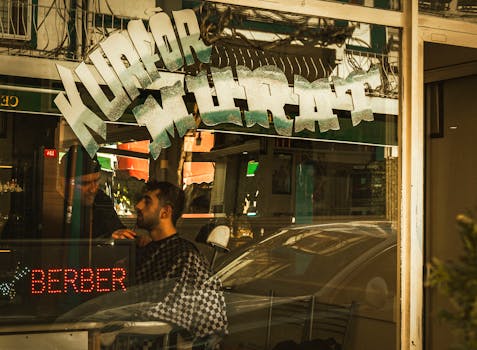 Man getting a haircut in a barbershop with reflective window signage.