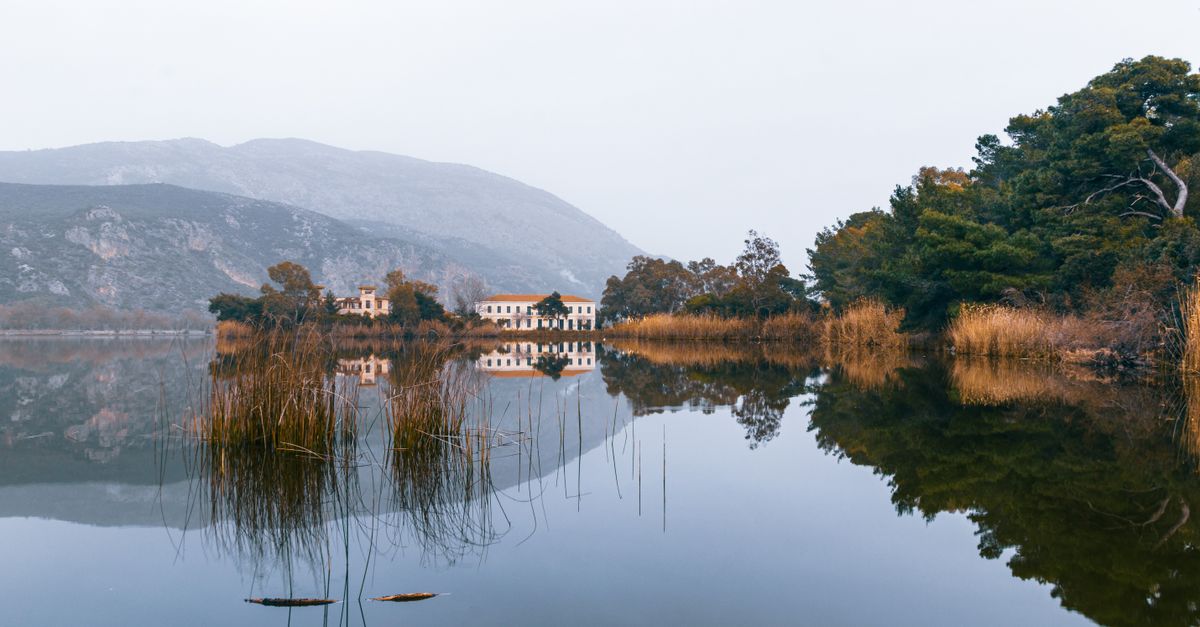 Tranquil autumn scene at Kaiafas Lake with foggy reflections, trees, and mountains.