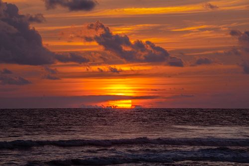 Free Dramatic sunset casting vibrant hues over ocean waves, creating a serene coastal scene. Stock Photo