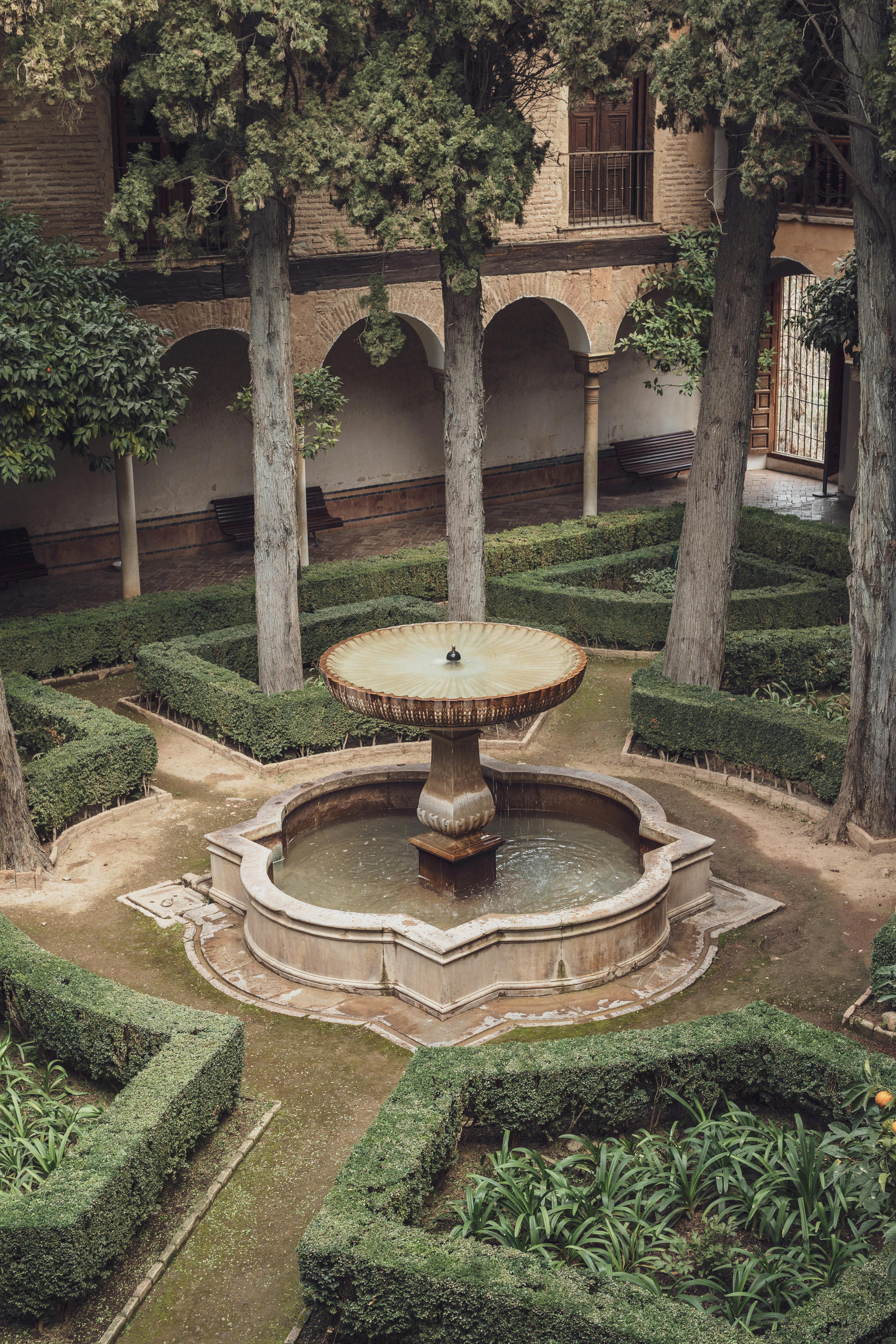 Serene courtyard with a central fountain and lush greenery in Alhambra, Spain.