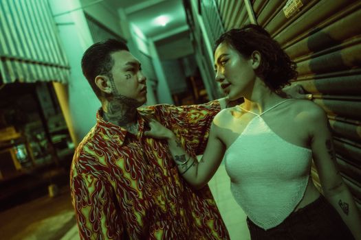 A tattooed couple shares an intimate moment on a city street at night, showcasing urban lifestyle.