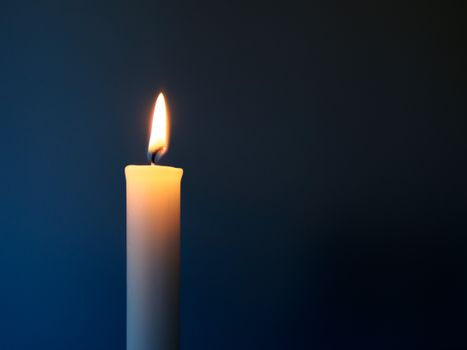 Burning white candle in front of a dark blue background