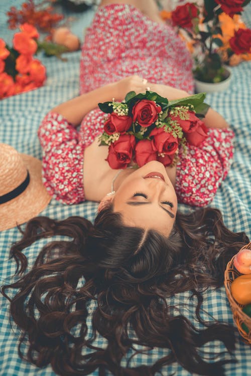 Long Haired Brunette Lying on a Picnic Blanket with a Bouquet of Red Roses in Hands