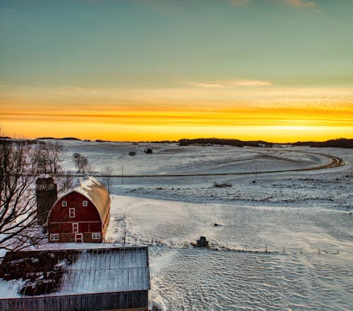 Aerial View of a Barn on a Snowy Field at Sunset 